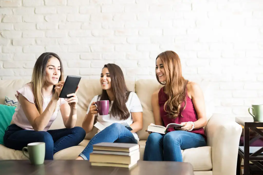 Three friends laughing and reading from paper books and eReaders