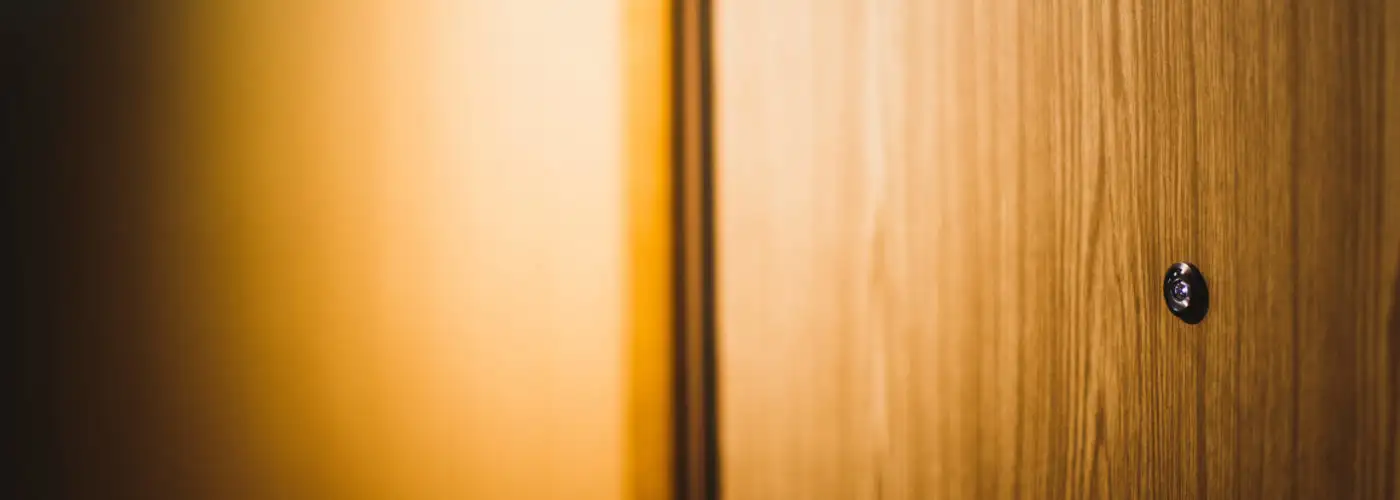 Warm toned image of a hotel room door with peephole in an orange hallway