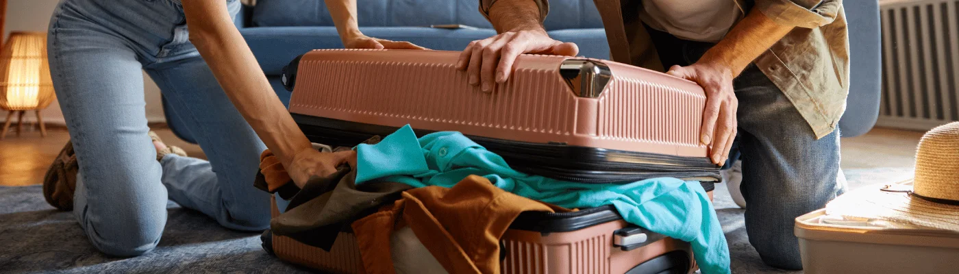 Couple trying to close luggage bag with excess of clothes